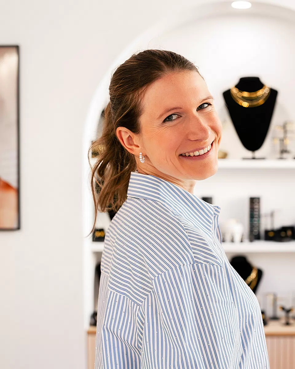 Aileen Nickel, Inhaberin von neelia, lächelnd in ihrem Laden vor einer Nische mit Ketten auf Schmuckbüsten